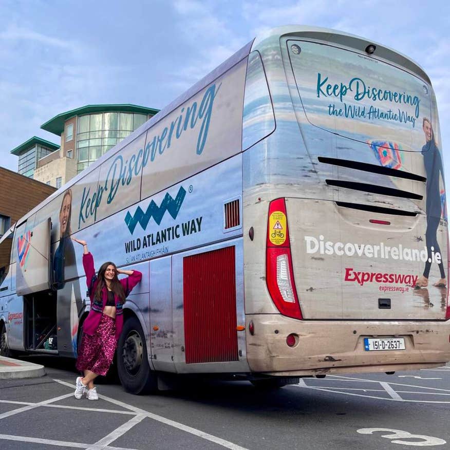 Woman in a pink leisure outfit leaning against the Keep Discovering Wild Atlantic Way Expressway bus.