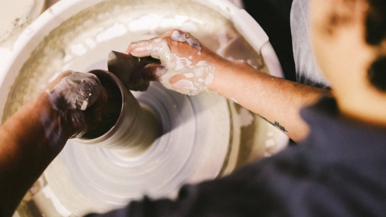 Looking down at potter's wheel with hands forming a tall pot.