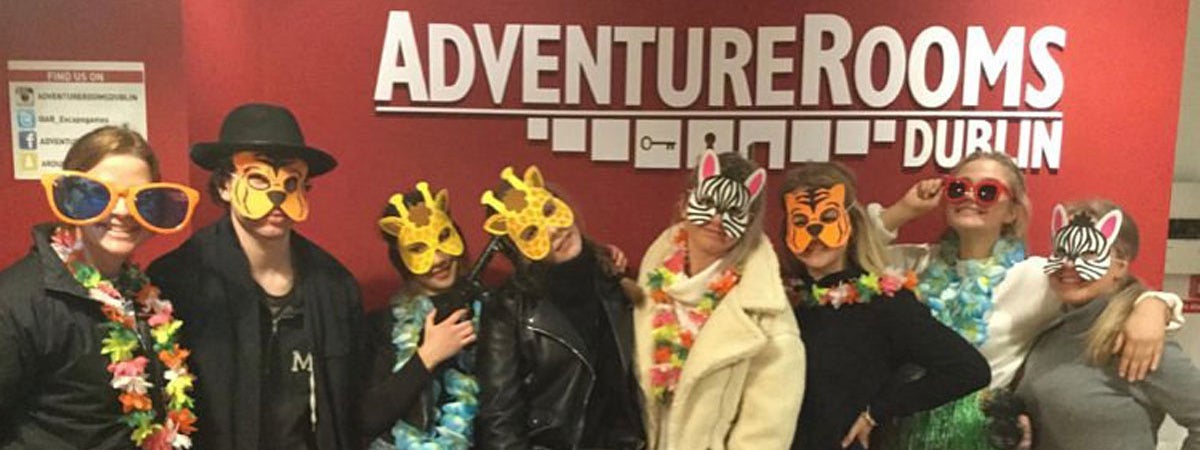 A group of people with animal masks and coloured sunglasses smiling into the camera standing under the Adventure Rooms logo