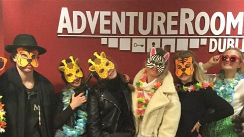 A group of people with animal masks and coloured sunglasses smiling into the camera standing under the Adventure Rooms logo