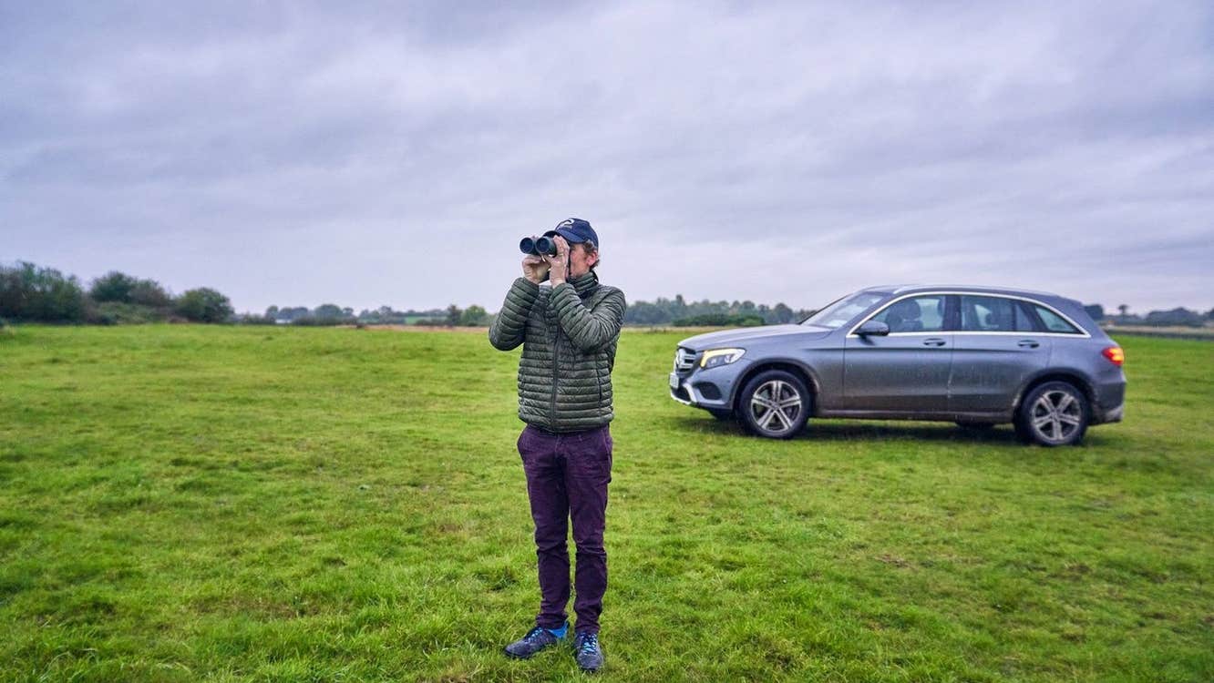 A man standing in a meadow looking through binoculars