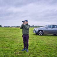A man standing in a meadow looking through binoculars