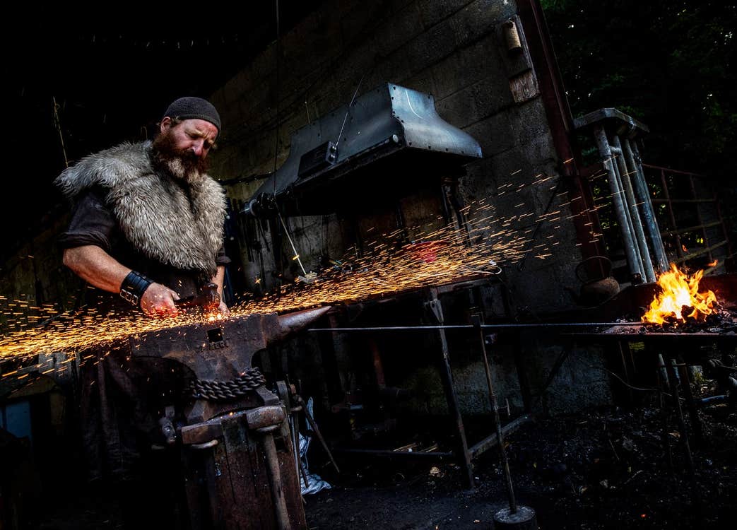 A man in period costume working in a forge with a hammer and anvil
