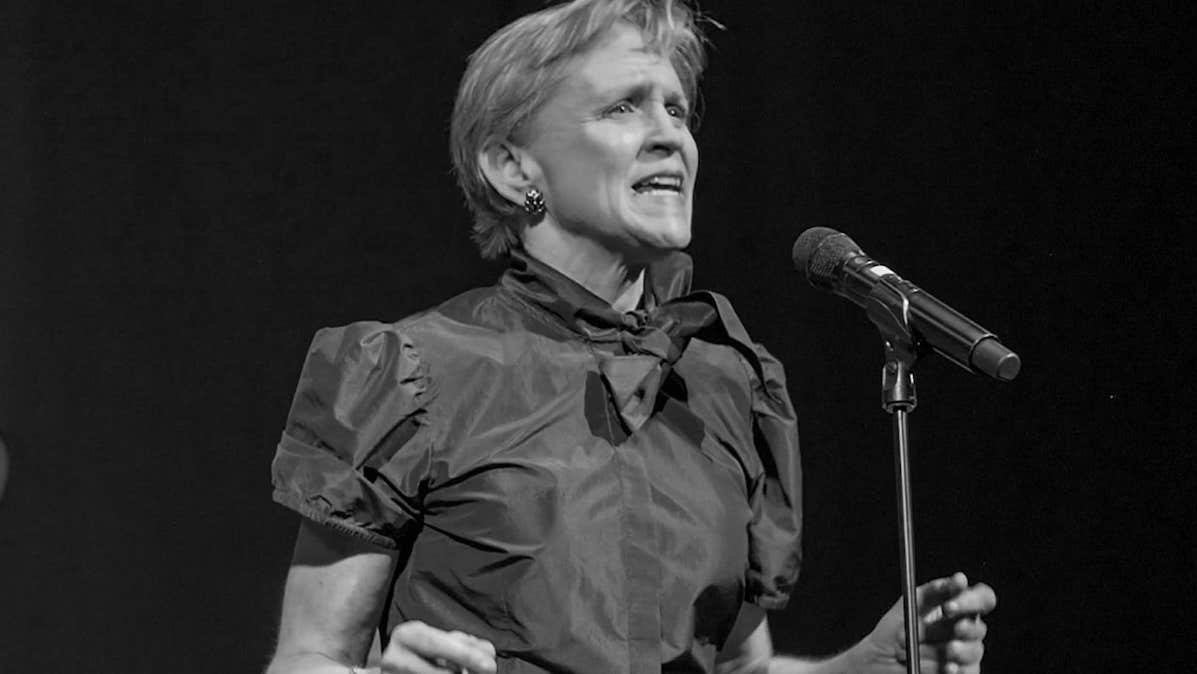 Black and white photo of woman singing with feeling into a mic on a stand.