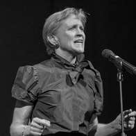 Black and white photo of woman singing with feeling into a mic on a stand.