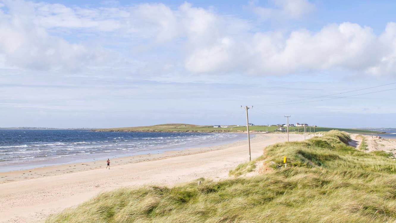 A sandy beach with grassy dunes and bright blue water lapping the shores.