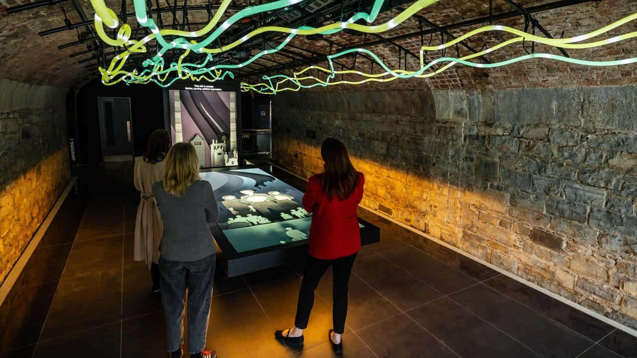 An interactive display table in a stone vaulted room with illuminated rope lighting along the ceiling