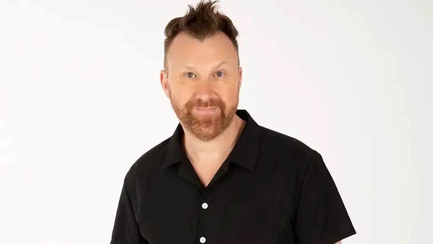 Smiling man in dark shirt against white background.