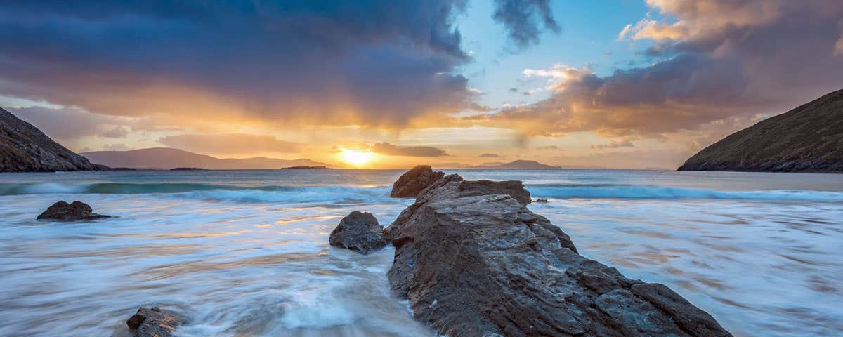 An atmospheric photo of a beach scene at sunrise or sunset with foaming sea around a large rock on a sandy beach