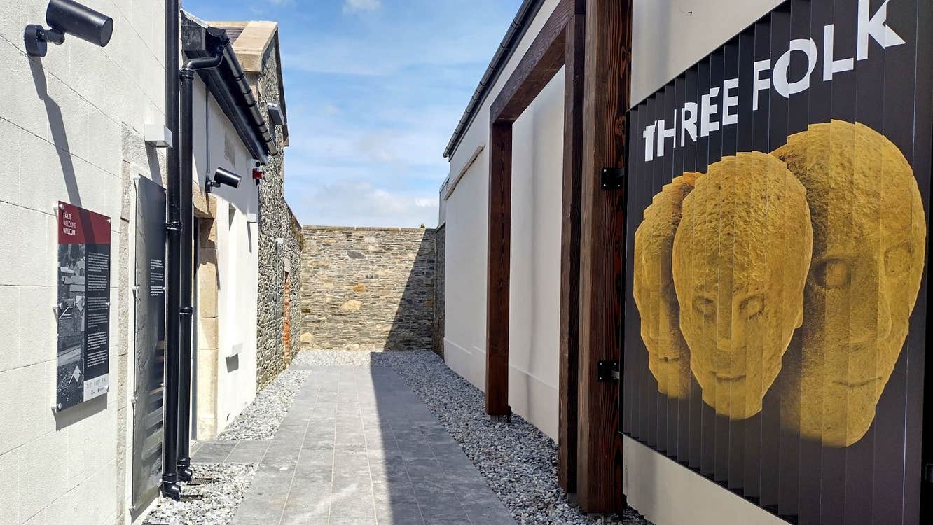 An alleyway with an entrance to a visitor centre with a large wall mural of three stone heads