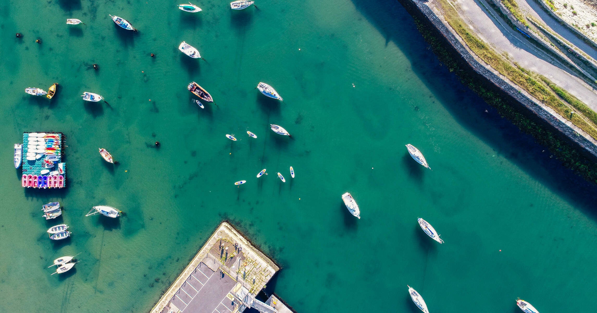 An aerial shot of the Dún Laoghaire Marina with different boats as well as people SUPing.