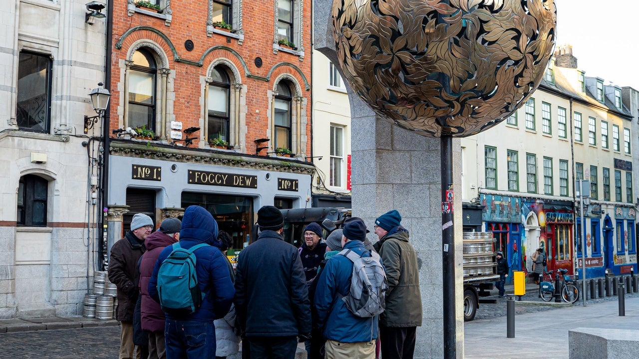 Group of people standing in a circle on a street listening to a guide with a gold globe above them