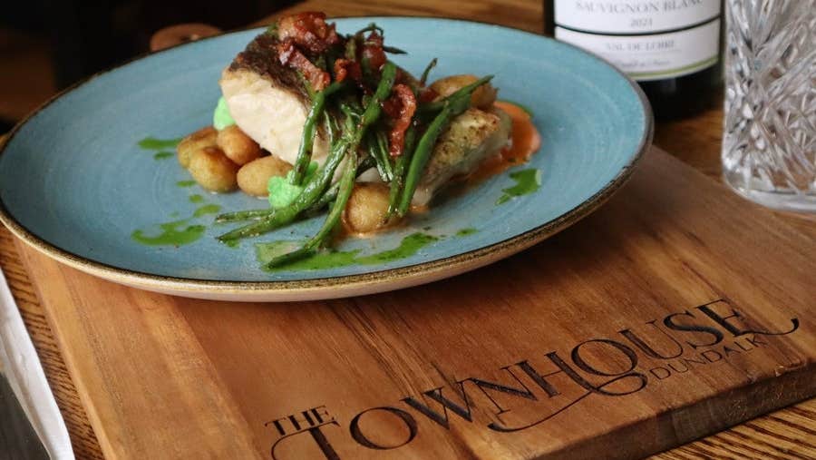 A chicken dish on a plate resting on a wooden slab with a restaurant name on it