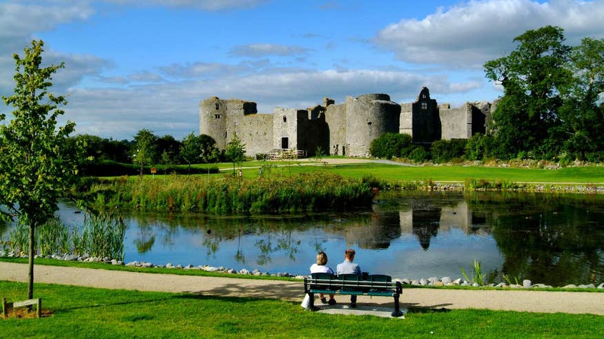 Two people sitting on a bench in front of a lake at Roscommon Castle