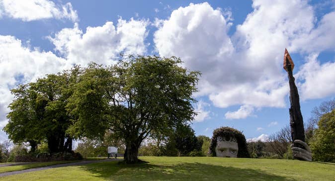 Green field with a giant head poking up from the ground holding a very tall spear