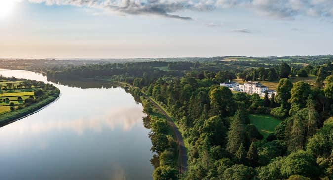 Aerial view of large estate house surrounded by trees and a lake in front