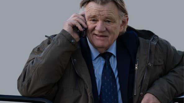 An older man in suit and tie with bulky overcoat is talking on a mobile