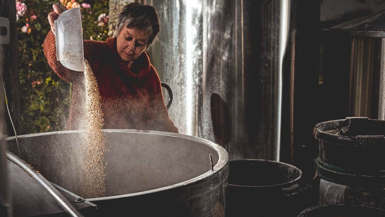 Someone pouring grains into a large vat in a brewery