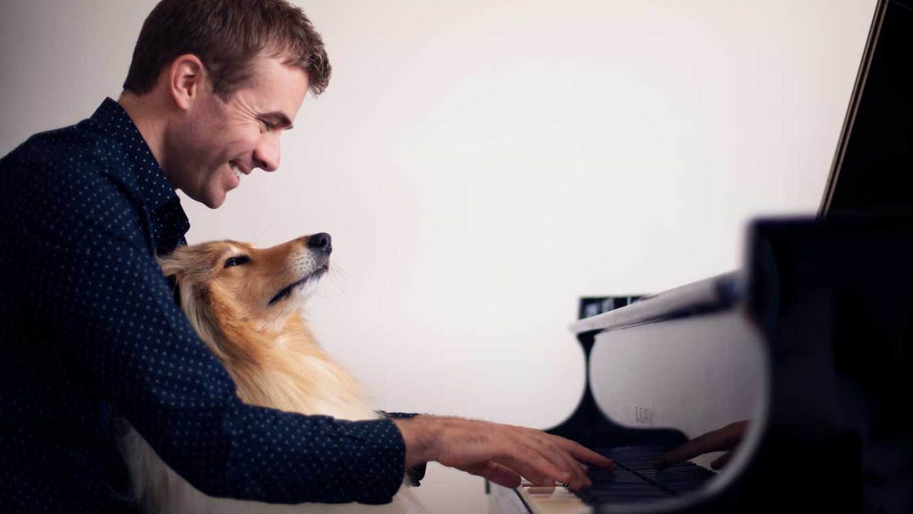 Fiachra Garvey piano recital Thomastown Concert Hall 8 February 2026 - side view of a smiling man seated at piano keyboard with dog on his lap