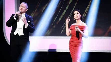 Gods, Monsters and Opera! Lú Festival of Light. A man and woman in evening dress holding mics, singing.