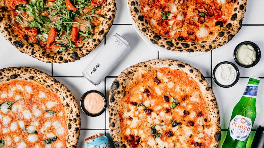 Four pizzas on a table with dips and drinks