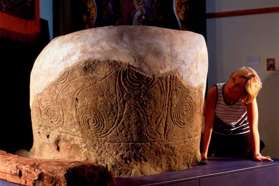 A woman looking closely at an artistic engraving on a stone.