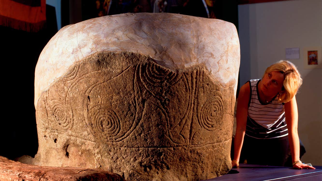A woman looking closely at an artistic engraving on a stone.
