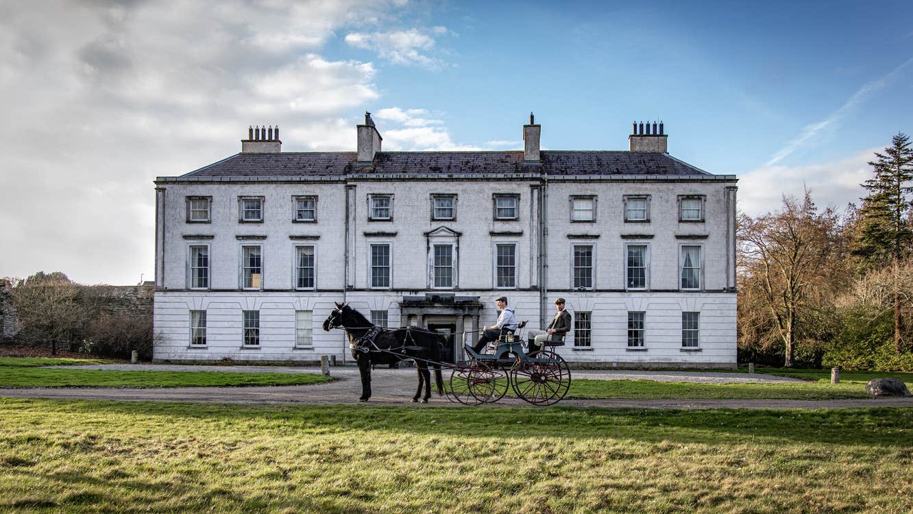 The exterior of a large country house with a horse and carriage outside the entrance