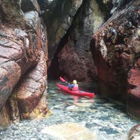 Sea Kayaking Donegal kayaker on the water near a colourful rocky inlet