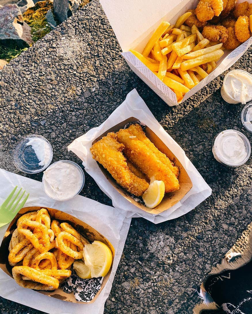 Three containers of fried fish and chips with small tubs of dips