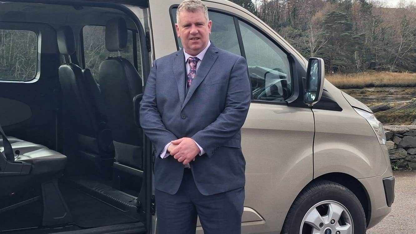 A chauffeur in a suit posed at his mini van