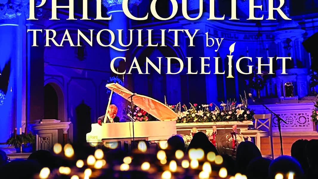A man in the background playing a pale coloured grand piano with blurry lit candles in the foreground.