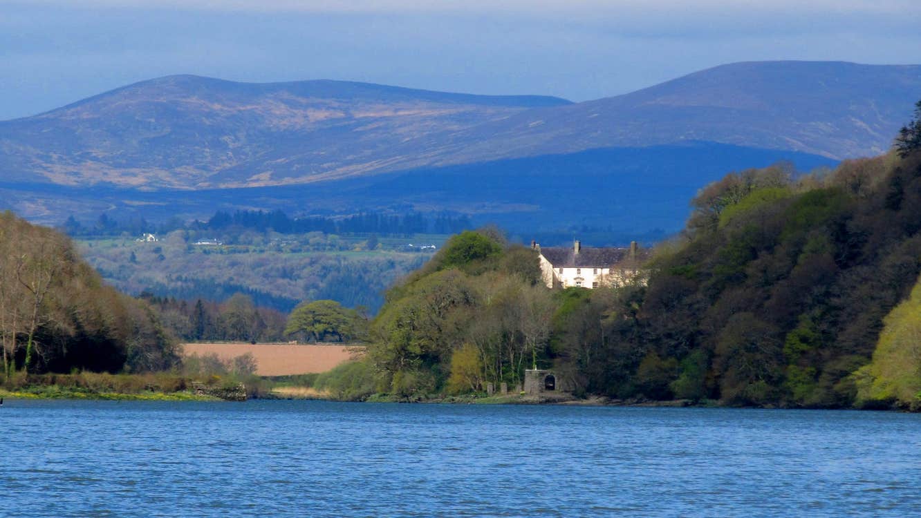 A large period house in the distance surrounded by trees overlooking the sea