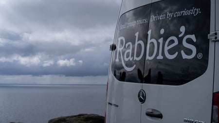 A small tour bus with a business logo parked beside the coast