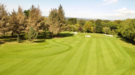 A view of Edmondstown Golf Club's course surrounded by trees under a blue sky