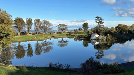 A clear lake surrounded by green trees reflects the blue sky above