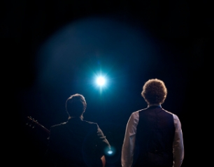 2 figures seen from behind looking forward at a single bright light against a dark background.