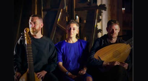 3 people looking serious sat in a line holding musical instruments, dimly lit.