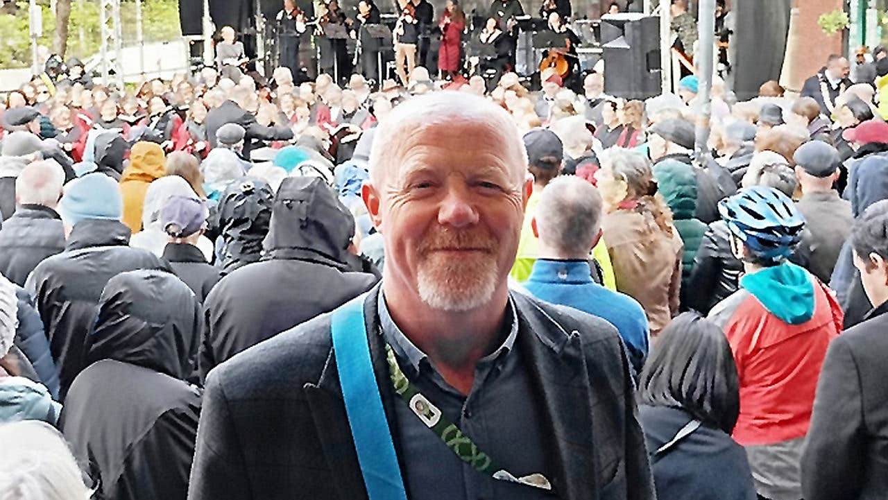 A person standing in front of a large outdoor crowd gathered at a stage with musicians performing