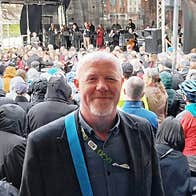 A person standing in front of a large outdoor crowd gathered at a stage with musicians performing