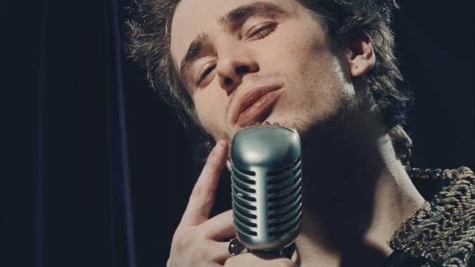A man singing into large old style mic with eyes shut.