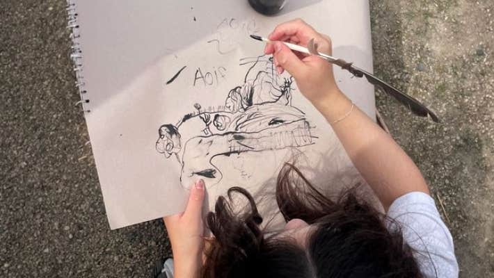 Looking down at young child holding a pen creating a black pen and ink picture.