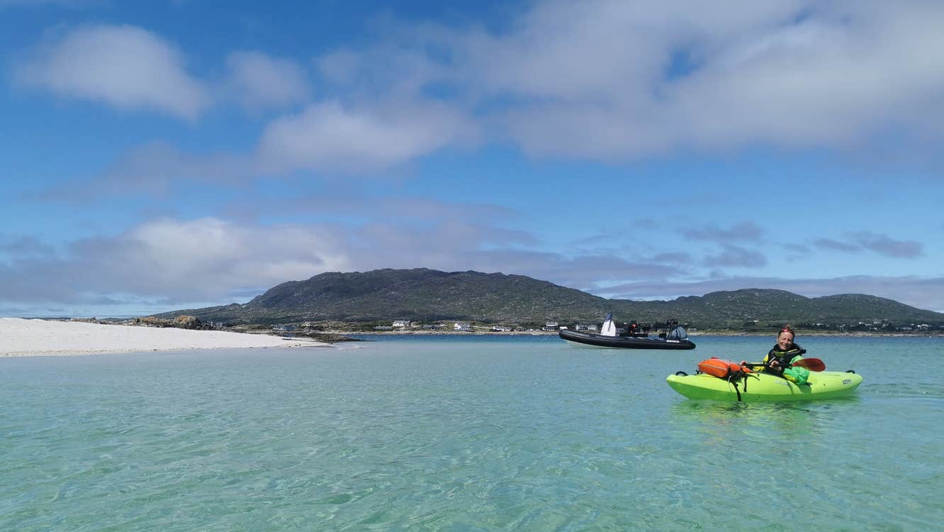 Person in a green kayak at sea near a sandy beach and green landscape