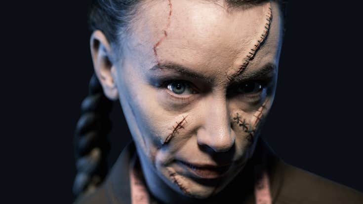 A woman with scarred SFX makeup looks sinisterly into the camera
