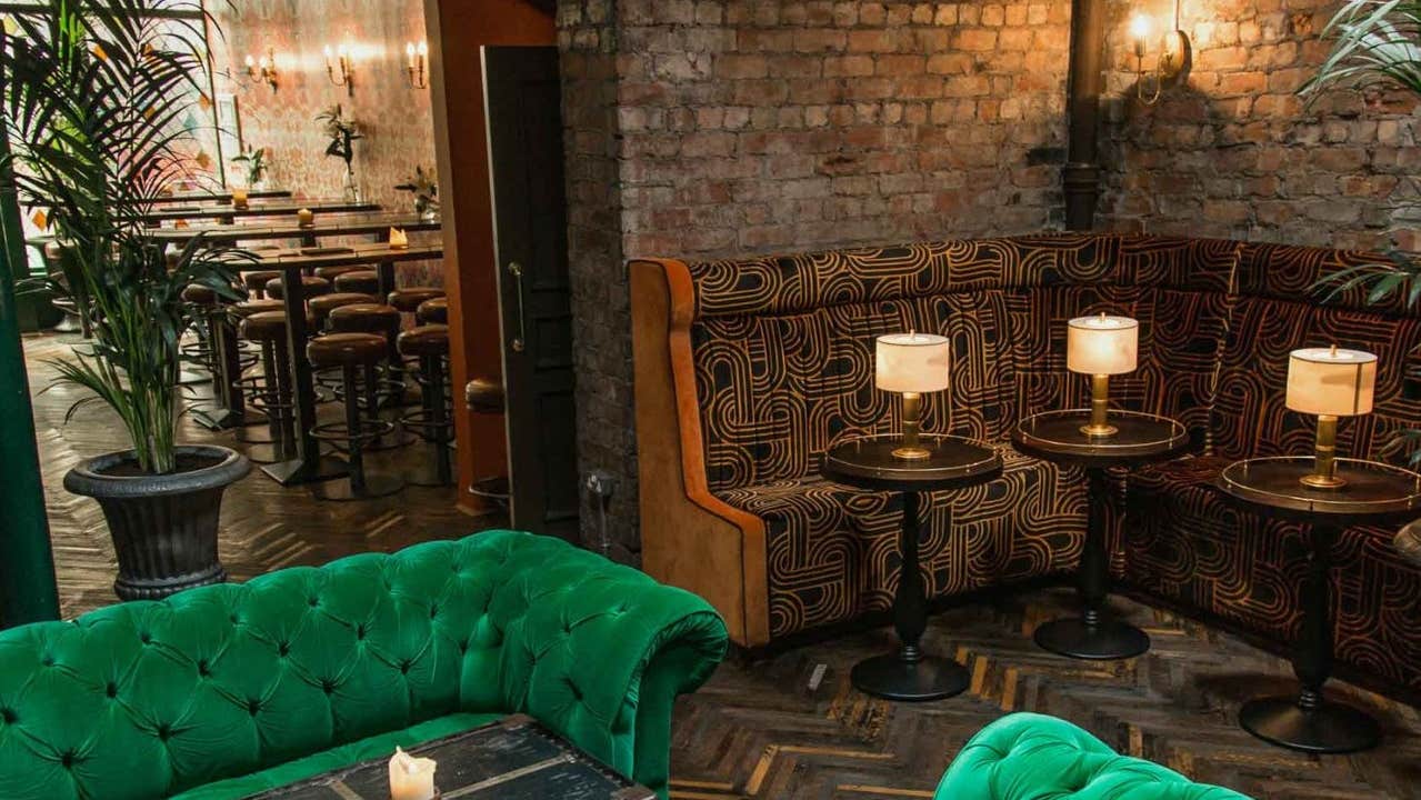 Green velvet seating area in an inviting lounge with candlelit tables and exposed brick walls
