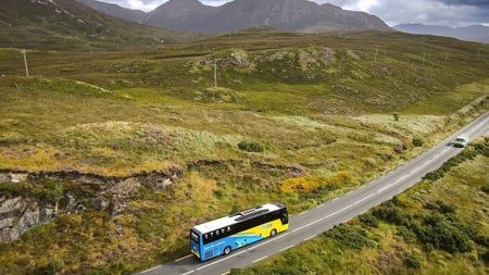 A blue and yellow coloured bus driving through Connemara countryside