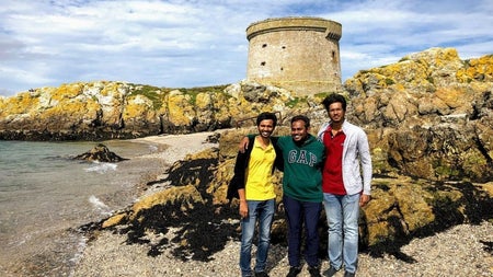 Three visitors standing on a rocky beach beneath a historic Martello Tower