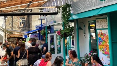 People standing and sitting outside a colourful café on the street