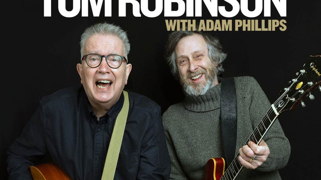 2 laughing older men both strumming guitars.