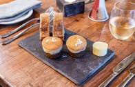 Bread and cakes on a slate plate on a table with cutlery and a wine glass in view